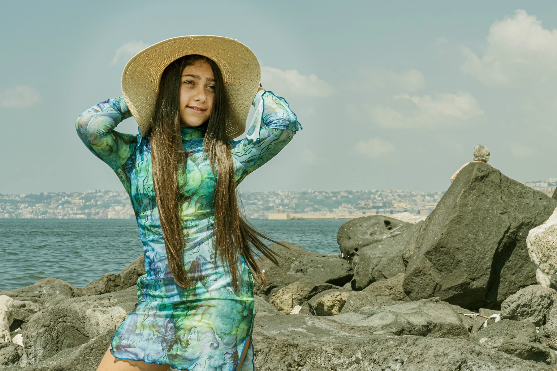 Bambina con cappello tra gli scogli sul mare