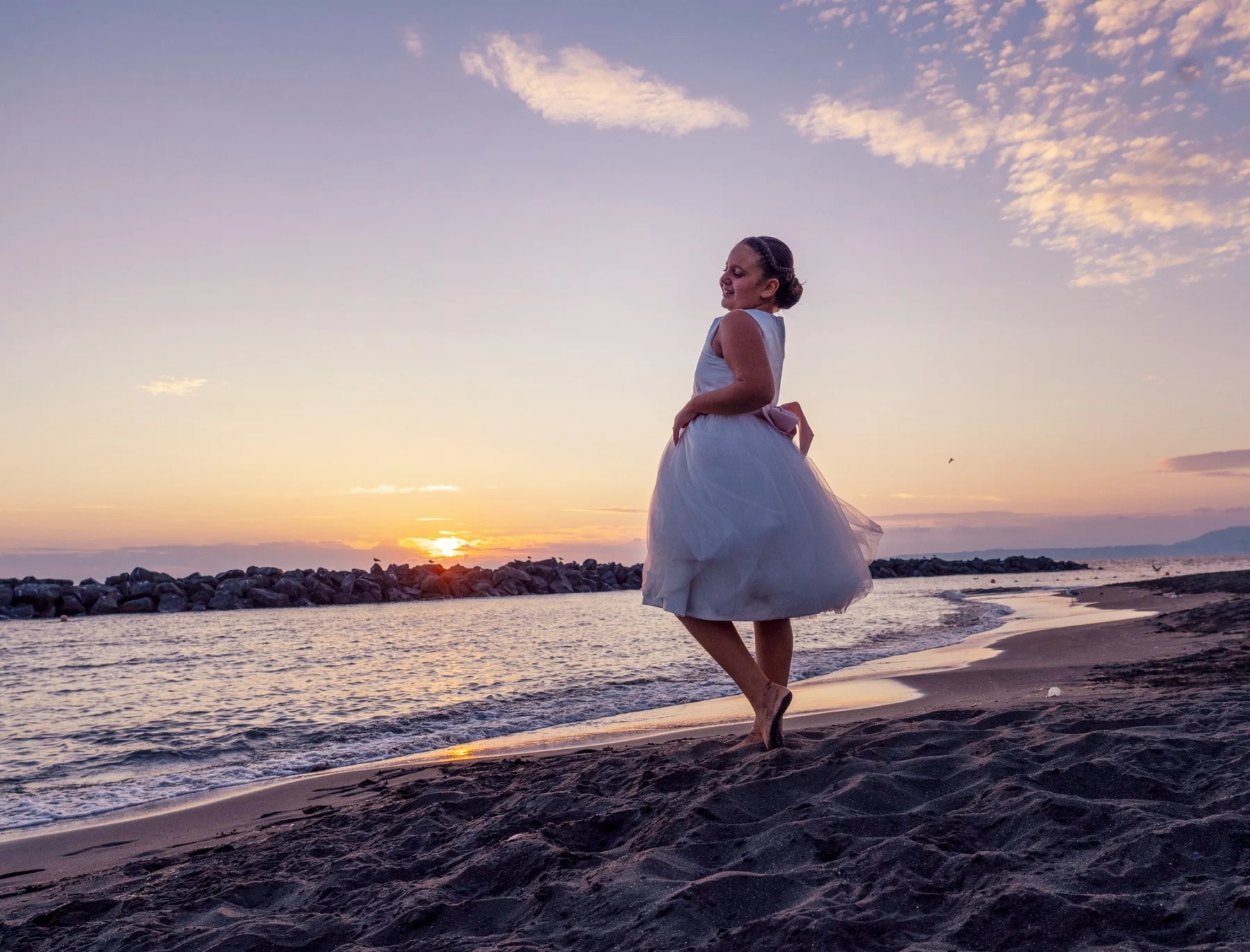 Bambina in abito da comunione sulla riva al tramonto