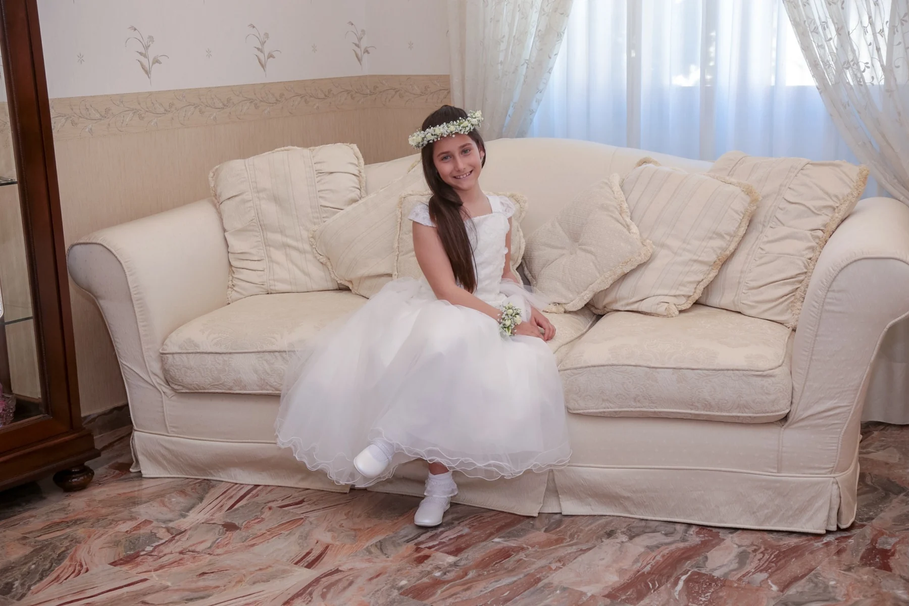 Bambina in abito da comunione seduta sul divano